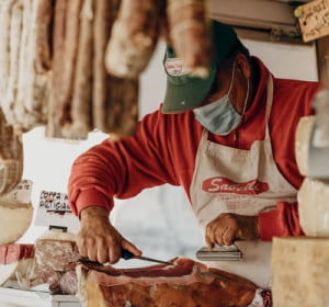 Slaktare som skär salami i deras Gastronomi med en covid mask.